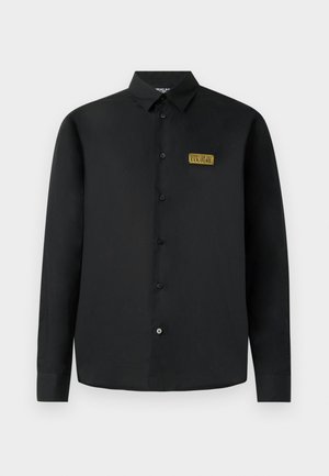 Melnas garās piedurknes pogājamās krekls ar apkakli un zelta taisnstūra Versace Jeans Couture logo uz kreisā krūšu kabatas.