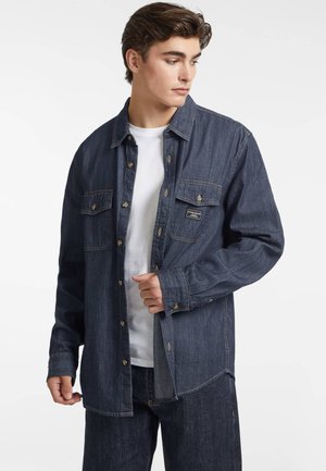 Denim shirt in dark blue with a button-up front, two chest pockets, and long sleeves. Features gold-tone hardware and contrast stitching.