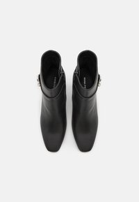 Czarne skórzane botki za kostkę z ostrym noskiem, o gładkiej fakturze, z ozdobnym srebrnym akcentem na boku.