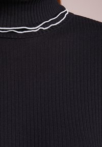 Col roulé côtelé noir avec des accents de passepoil blanc le long du col. Vue rapprochée mettant en valeur la texture et les caractéristiques du design.