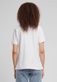 Hvid kortærmet t-shirt med en afslappet pasform. Simpelt design, blødt bomulds materiale, ingen mønstre. Set fra bagsiden, parret med lyseblå bukser.