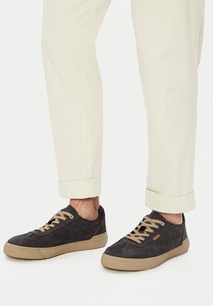 Sneakers in suede nero con punte rotonde, suole di gomma beige e lacci a contrasto. Indossate con pantaloni chiari risvoltati.