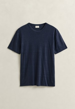 T-shirt à manches courtes, col rond, bleu marine, en tissu léger, posé à plat sur un fond beige.