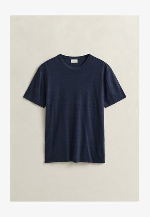 T-shirt à manches courtes, col rond, bleu marine, en tissu léger, posé à plat sur un fond beige.