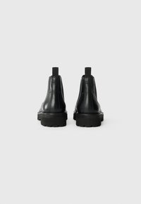 Botas de tobillo de cuero negro con un acabado mate, paneles laterales elásticos y suelas gruesas de goma con un dibujo profundo para mayor tracción.