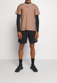 Atuendo deportivo de Nike que incluye una camiseta corta marrón con detalles negros, combinada con pantalones cortos negros y zapatillas deportivas negras.