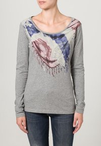 Graues Langarmshirt mit einem mehrfarbigen geometrischen Design am Ausschnitt, verziert mit Fransen und Farbspritzern.