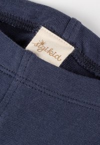 Tessuto di cotone blu navy con una superficie liscia e cuciture visibili, caratterizzato da un'etichetta tessuta di colore crema con la scritta "sigikid" stampata in marrone.