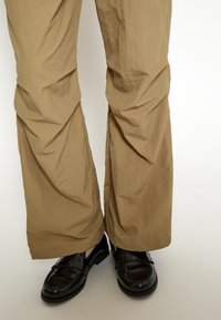 Pantaloni beige leggeri con una texture increspata e una vestibilità rilassata, abbinati a mocassini neri lucidi.