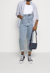 Světle modrá lněná košile, bílý tričko, džíny s vysokým pasem ve světle modré barvě, černobílé tenisky, malá námořnická taška s červeným zipem.