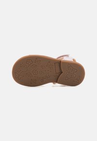 Rosa sandaler med en brun gummisåle. Har blomster- og sommerfuglmønstre på sålen. Velcro-stropper gir enkel festing.