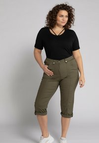 Haut noir à manches courtes avec des bretelles au cou, associé à un pantalon cropped vert olive doté de poches avant et de poignets retroussés ; porté avec des baskets blanches.