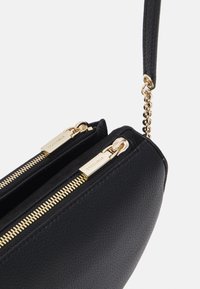 Borsa a tracolla nera in pelle con due cerniere, hardware dorato, superficie texturizzata e una tracolla corta decorata con dettagli in catena.