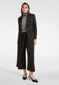 Zwarte pinstriped blazer met dubbele knopen, grijze coltrui, wijde zwarte broeken en zwarte slingback hakken met strikaccenten.
