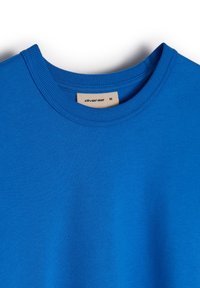 Niebieska koszulka z krótkim rękawem, uszyta z gładkiej bawełny, z żebrowanym dekoltem okrągłym i metką z napisem "diverse" oraz rozmiarem "M".