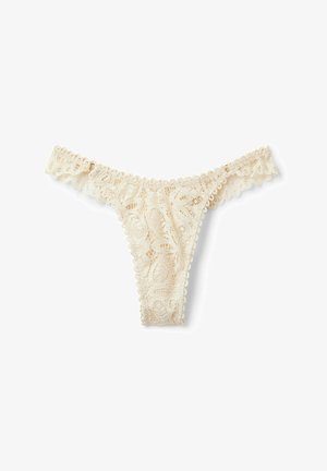 String en dentelle de couleur crème avec motif floral. Les bords festonnés et la texture douce améliorent le design. Convient pour être porté sous les vêtements.