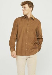 Chemise boutonnée marron en tissu texturé, avec un col classique, des manches longues et une poche poitrine unique.