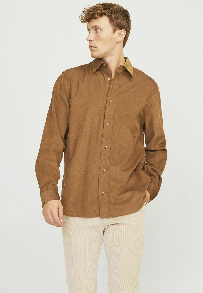 Chemise boutonnée marron en tissu texturé, avec un col classique, des manches longues et une poche poitrine unique.