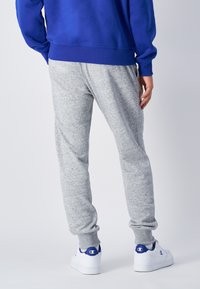 Grå mjukisbyxor med manschett vid anklarna, gjorda av ett mjukt, texturerat tyg. Matchade med vita sneakers med blå detaljer.