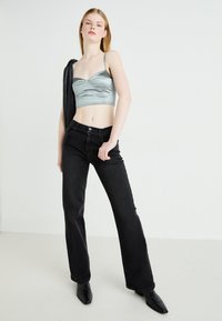 Top cropped in satin argento con spalline sottili, abbinato a jeans flare neri in denim a vita alta e stivaletti neri con punta.