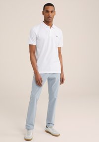 Camiseta polo blanca con un pequeño logo negro, combinada con pantalones azul claro y zapatillas blancas. Presenta un cuello clásico y mangas cortas.