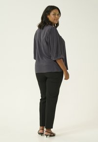Blusa a pois blu navy con maniche a 3/4, texture morbida, abbinata a pantaloni neri aderenti e tacchi neri a strappo, vista da dietro.