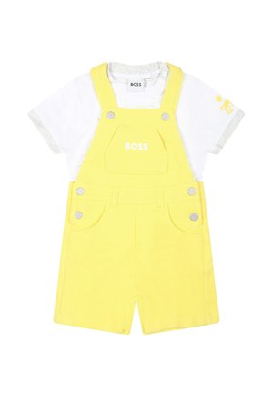 Gele katoenen korte tuinbroek met zilverkleurige details en een voorzak, gecombineerd met een witte T-shirt met grijze accenten en logo.