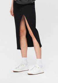 Czarna midi spódnica z bocznym rozcięciem, o dopasowanym kroju. Połączona z białymi trampkami i skarpetkami typu crew, co podkreśla swobodny wygląd.