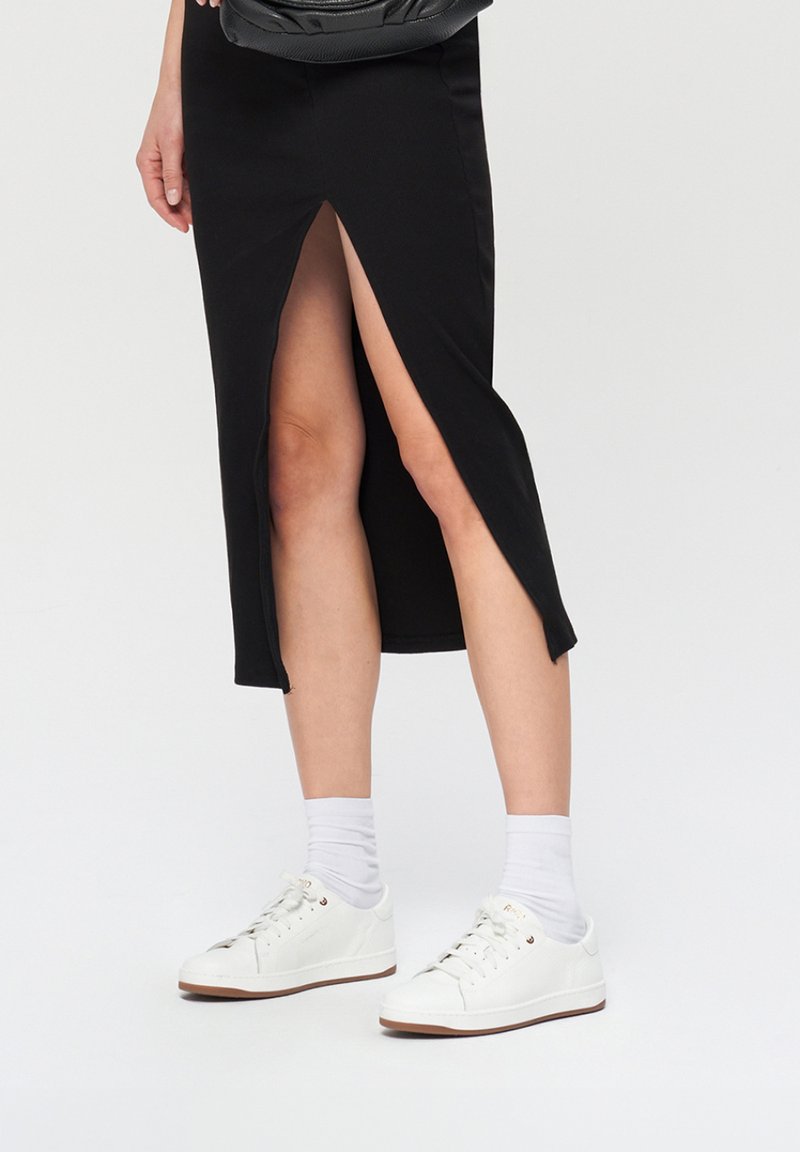 Czarna midi spódnica z bocznym rozcięciem, o dopasowanym kroju. Połączona z białymi trampkami i skarpetkami typu crew, co podkreśla swobodny wygląd.