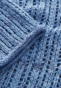 Tessuto lavorato a maglia azzurro chiaro con una trama aperta e testurizzata. Presenta un design a anelli e un'accenno di blu leggermente più scuro lungo il bordo.
