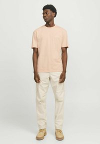 Lichtroze katoenen T-shirt met korte mouwen en een ronde hals; gecombineerd met beige cargobroek en beige laarzen, voorzien van dubbele zijzakken.