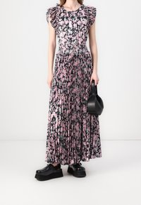 Valkoinen ja musta kukallinen mekko, jossa on rypytetty kaula-aukko, pleatattu hame ja musta käsilaukku. Mustat platform-kengät viimeistelevät asun.