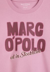 Felpa in cotone organico rosa con grande ricamo in lettere rosa scuro, "Marc O'Polo", con cuciture bianche su una superficie liscia.