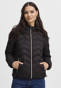 Črna puhovka s cik-cak vzorcem, z zapiranjem na zadrgo in nastavljivo kapuco. Na prednji strani sta dva žepa in elastični manšeti.