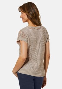 Beige gebreide trui met korte mouwen, met een opengewerkte structuur, geribbelde zoom en decoratieve details op de rug.