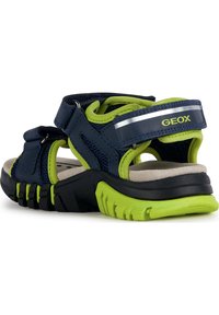 Navy blue sandals with green accents, featuring a mesh upper and adjustable straps. Rubber sole with a textured grip. Geox branding visible.