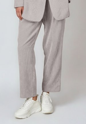 Lower half of person wearing light grey pinstriped pants and oversized blazer with white chunky sneakers against a plain background.