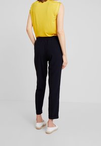 Gul ärmlös topp och marinblå byxor med elastisk midja, med uppvikta avslut. Modellen har på sig vita espadrillos. Enkla designdetaljer med en avslappnad passform.