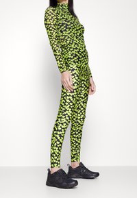 Długi rękaw body wykonane z przezroczystej czarnej tkaniny z wzorem małych zielonych serc; zestawione z czarnymi butami sportowymi.