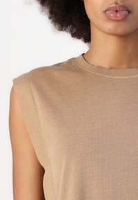 Top sin mangas marrón hecho de suave algodón; presenta un cuello redondo, una textura sutil y costuras limpias en los hombros.