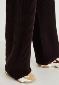 Pantalons large en tricot côtelé noir associés à des sneakers beige et blancs. Texture lisse avec une coupe ample et un design longueur sol.
