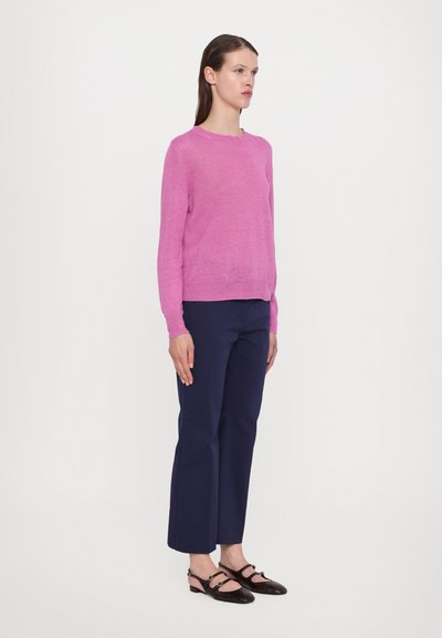 Maglione rosa chiaro a maglia con collo rotondo, abbinato a pantaloni cropped blu scuro e scarpe slingback nere con dettagli dorati.