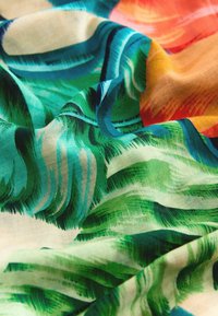 Tissu avec des motifs tropicaux de feuilles et de fleurs vibrants aux teintes vertes, bleues, orange et rouges, présenté avec des plis doux et de la texture.