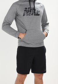 Sweatshirt à capuche gris avec logo Nike noir, poche kangourou ; associé à un short noir avec un logo subtil. Le matériau semble lisse et sportif.