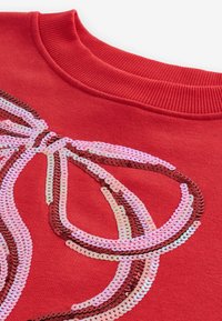 Červená mikina s multifarebnými flitry uspořádanými v vlnovém vzoru, s žebrovaným výstřihem a měkkou texturou.