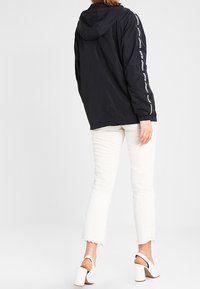 Czarna, lekka kurtka z kapturem, z białym logo wzdłuż rękawów. W połączeniu z białymi, krótkimi dżinsami i sandałami na słupku.