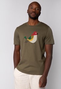 T-shirt en coton vert olive arborant un graphique stylisé d'oiseau en rouge, jaune, vert et noir. Manches courtes et col rond.