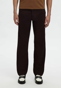 Zwarte rechte broek van gladde stof, met een minimalistisch ontwerp. Gepaard met zwart-witte schoenen met decoratieve accenten.