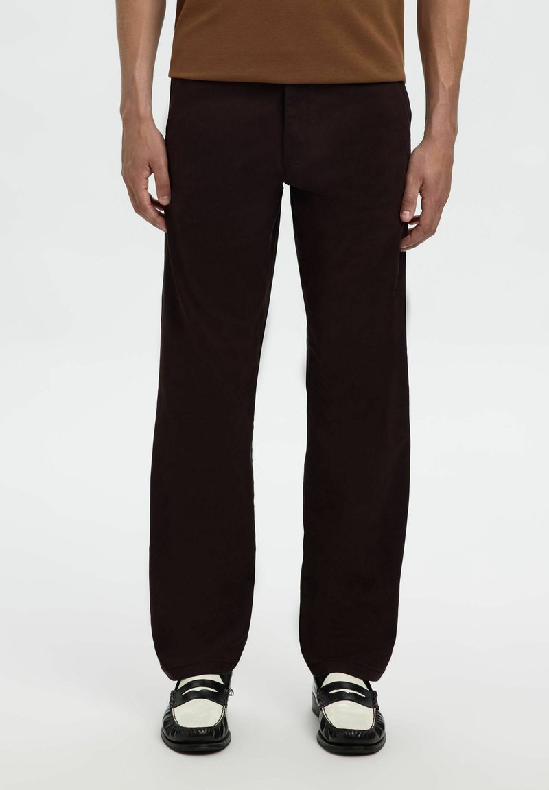 Zwarte rechte broek van gladde stof, met een minimalistisch ontwerp. Gepaard met zwart-witte schoenen met decoratieve accenten.