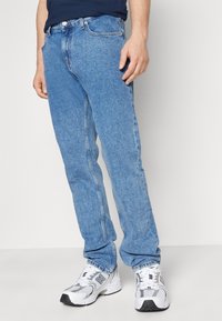 Ljusblå denimjeans med raka ben, femficksdesign och en diskret tvätt; bärs med vita sneakers med grå accenter.